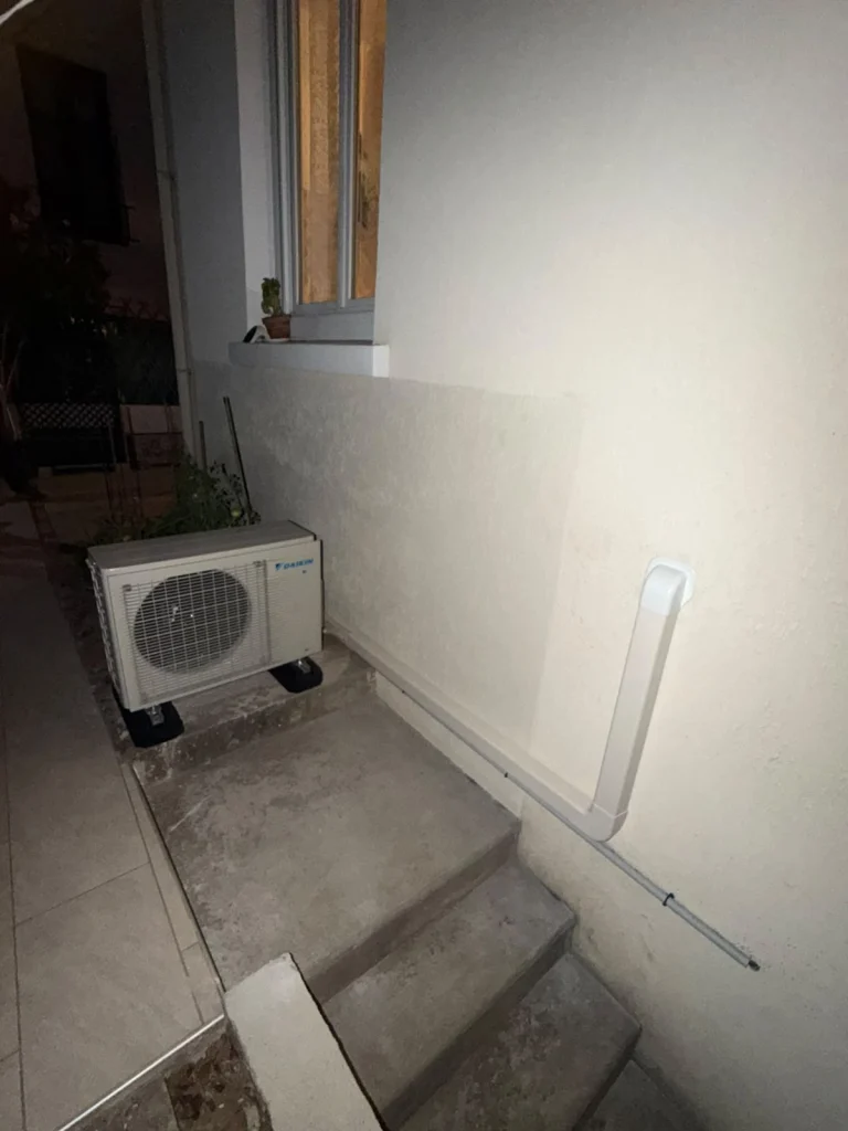 Groupe extérieur de climatisation installé sous un escalier extérieur, goulotte le long du mur, climaticien Île-de-France