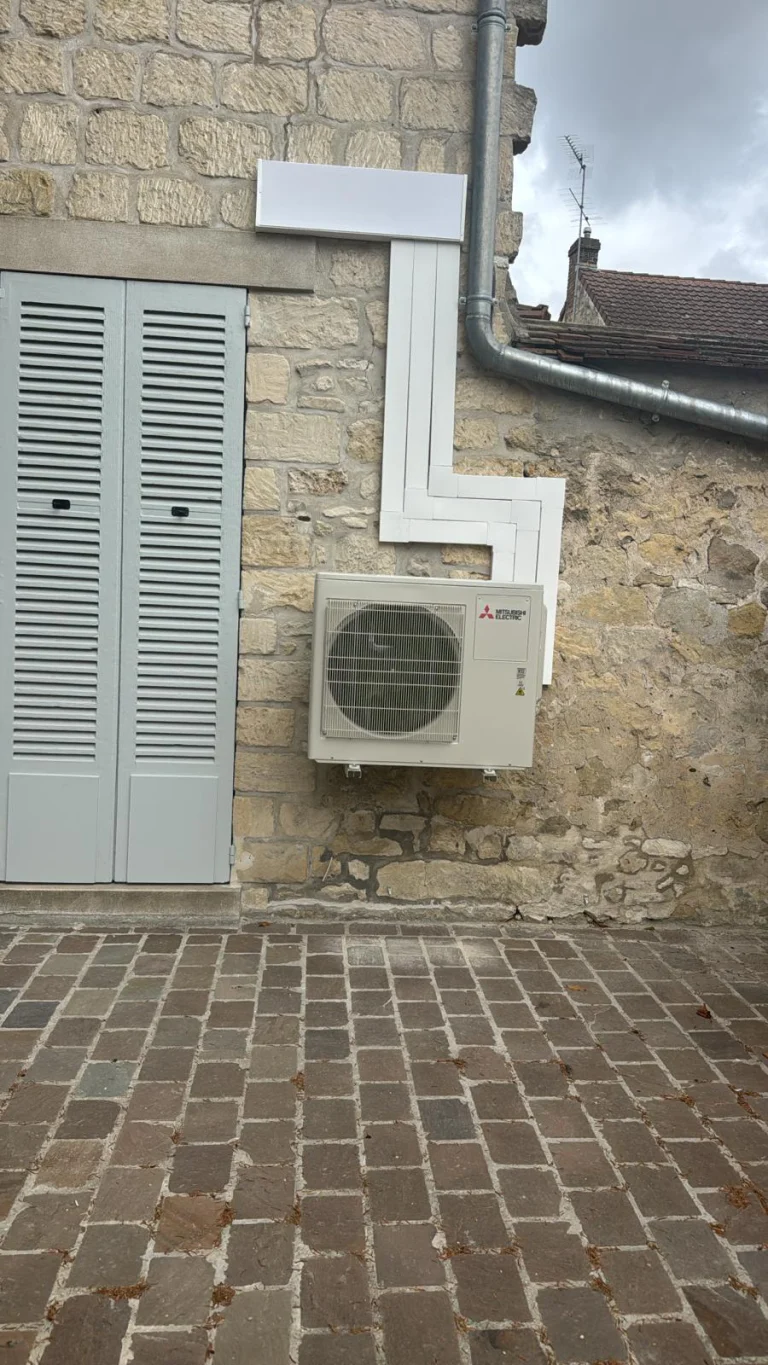 Groupe extérieur Mitsubishi Electric sur support mural et goulotte à angles droits sur une façade en pierre, climaticien Île-de-France