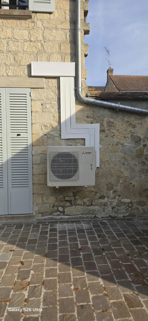 Groupe extérieur Mitsubishi Electric sur support mural et goulotte à angles droits sur une façade en pierre, climaticien Île-de-France