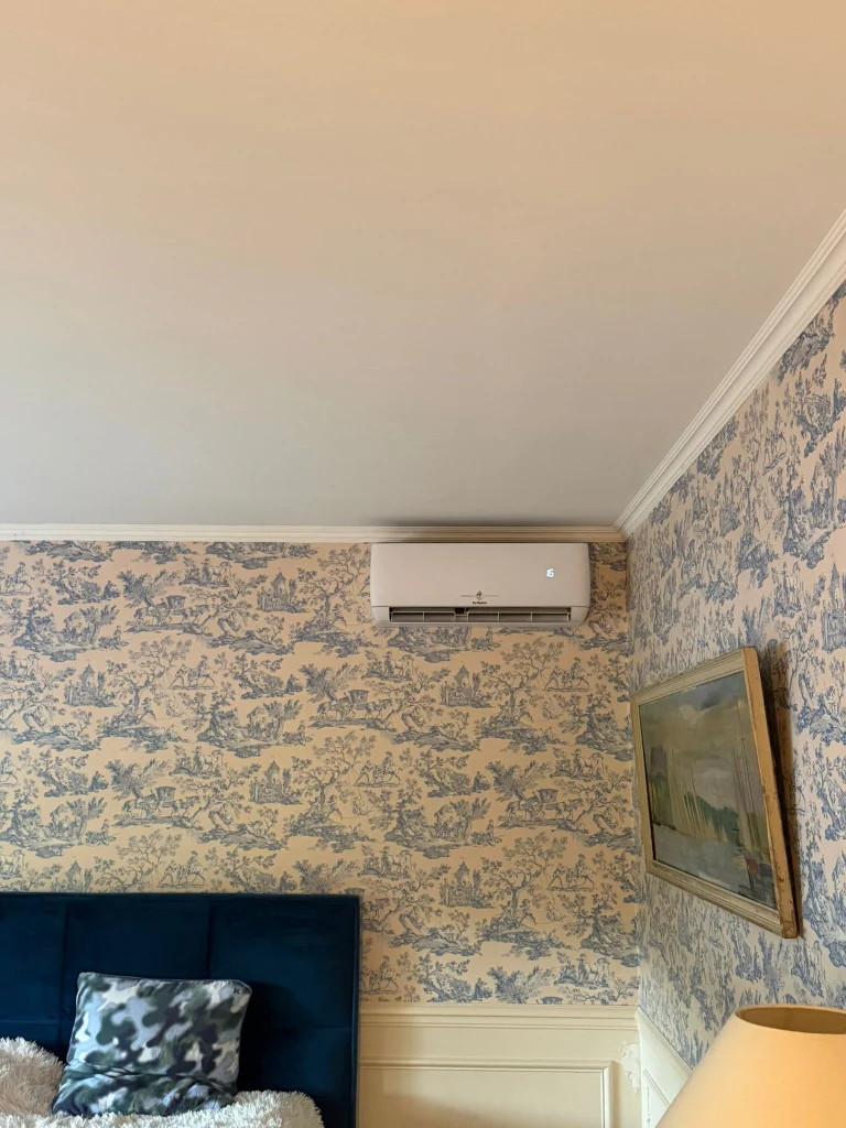 Split mural de climatisation installé dans une chambre au papier peint toile de Jouy, climaticien Île-de-France
