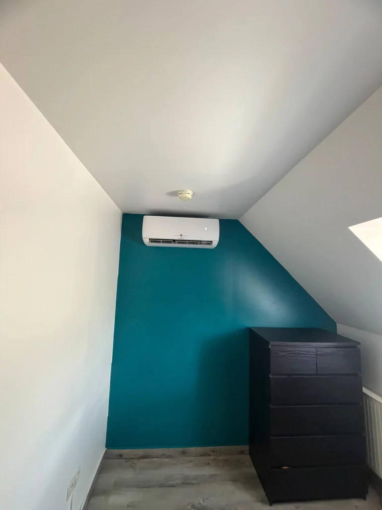 Split mural de climatisation sous rampant dans une chambre aux murs bleu canard, climaticien Île-de-France