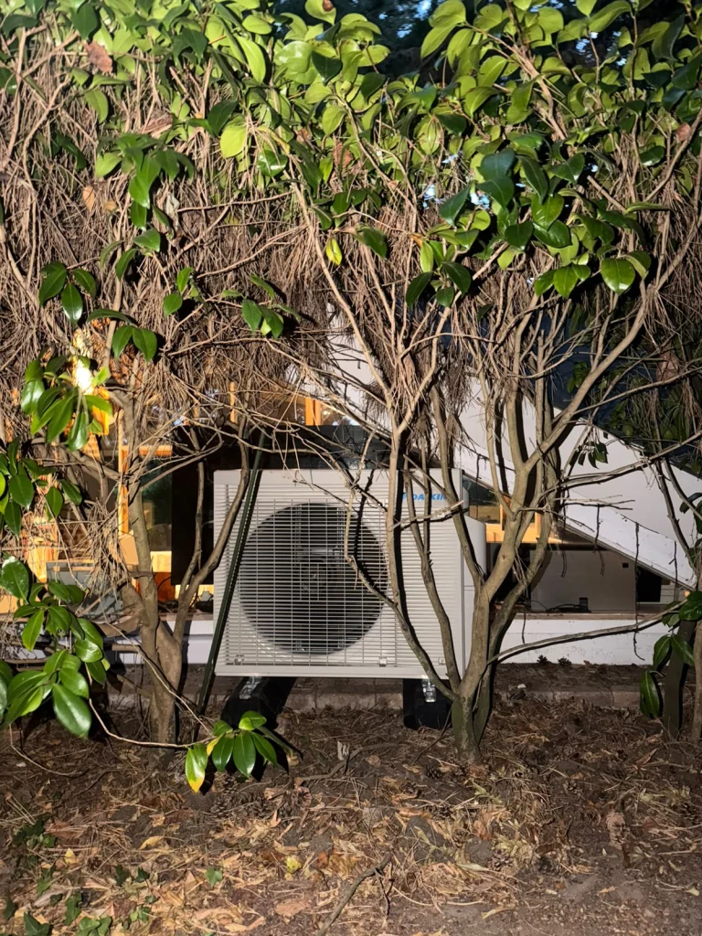 Groupe extérieur de climatisation intégré dans la végétation d'un jardin, climaticien Île-de-France