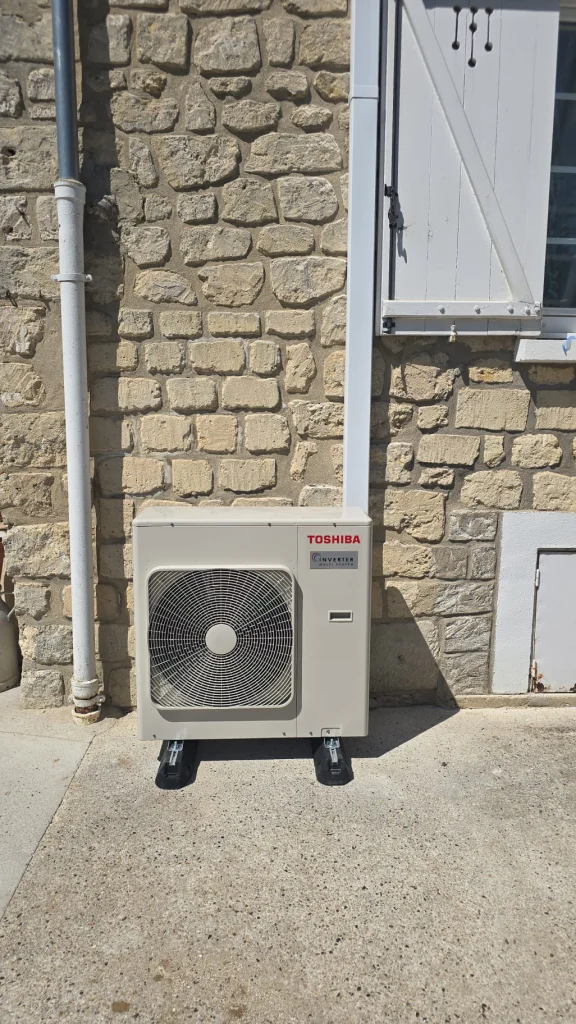 Groupe extérieur de climatisation Toshiba au sol devant une façade en meulière, climaticien Île-de-France