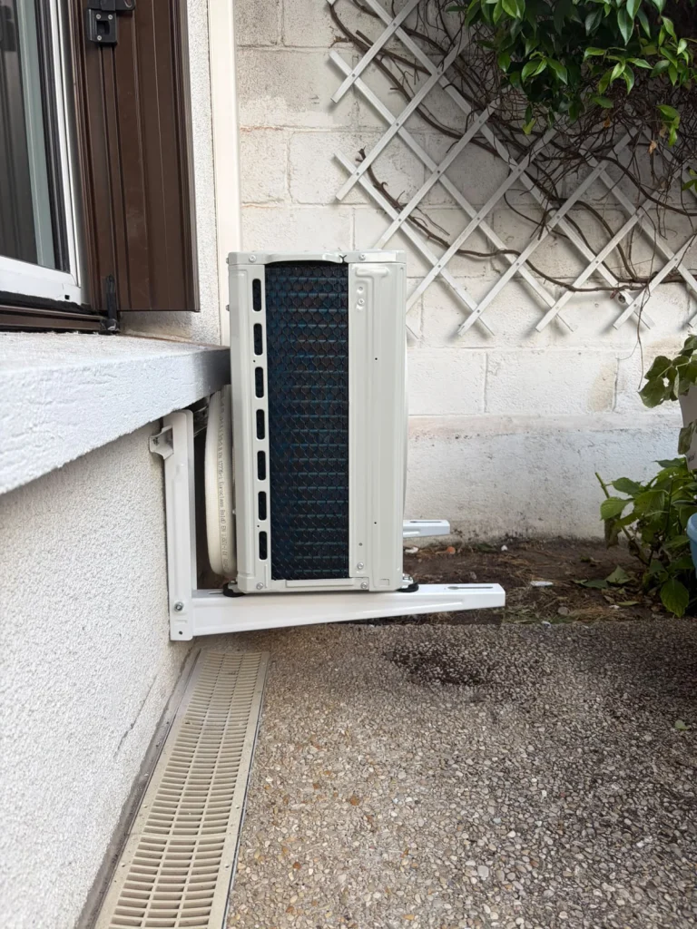 Deux groupes extérieurs de climatisation devant un treillage, au sol et sur support mural bas, climaticien Île-de-France