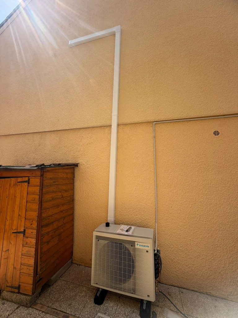 Groupe extérieur de climatisation au sol contre un mur ocre à côté d'un abri de jardin, climaticien Île-de-France