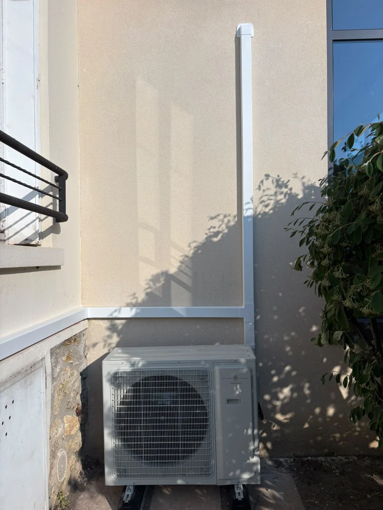 Groupe extérieur de climatisation au sol avec goulotte montante sur une façade grise, climaticien Île-de-France