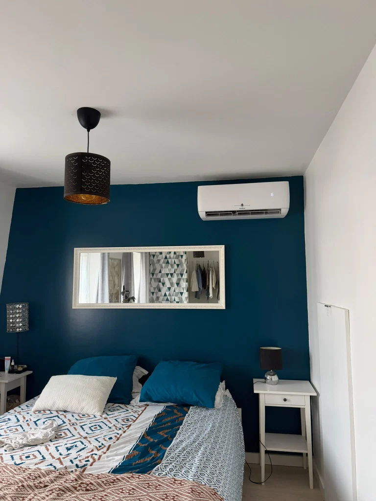 Split mural de climatisation réversible dans une chambre au mur bleu, climaticien Île-de-France