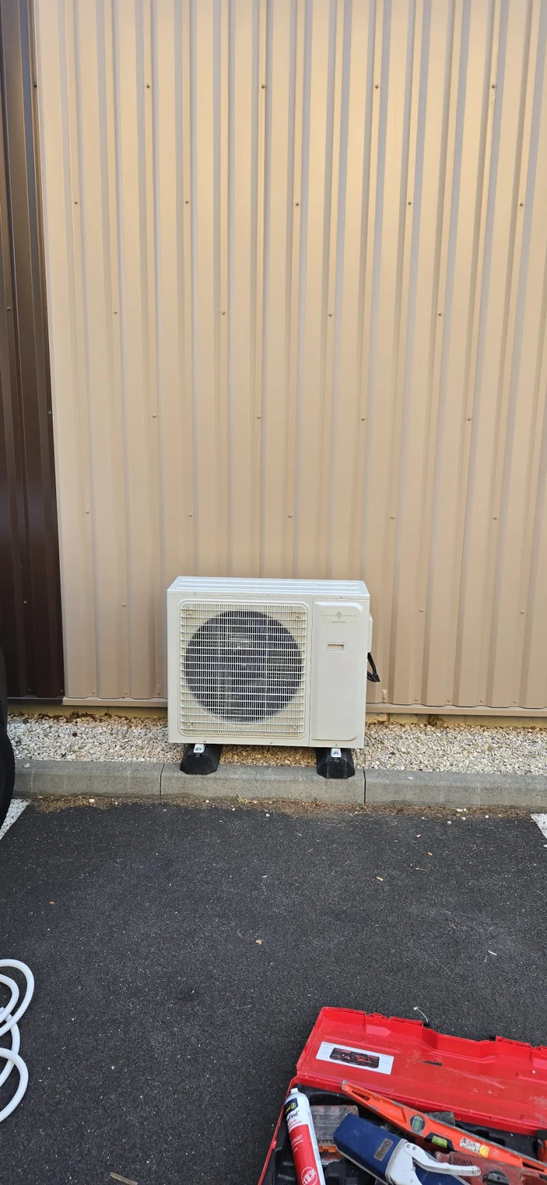Groupe extérieur de climatisation au sol devant le bardage métallique d'un local professionnel, climaticien Île-de-France