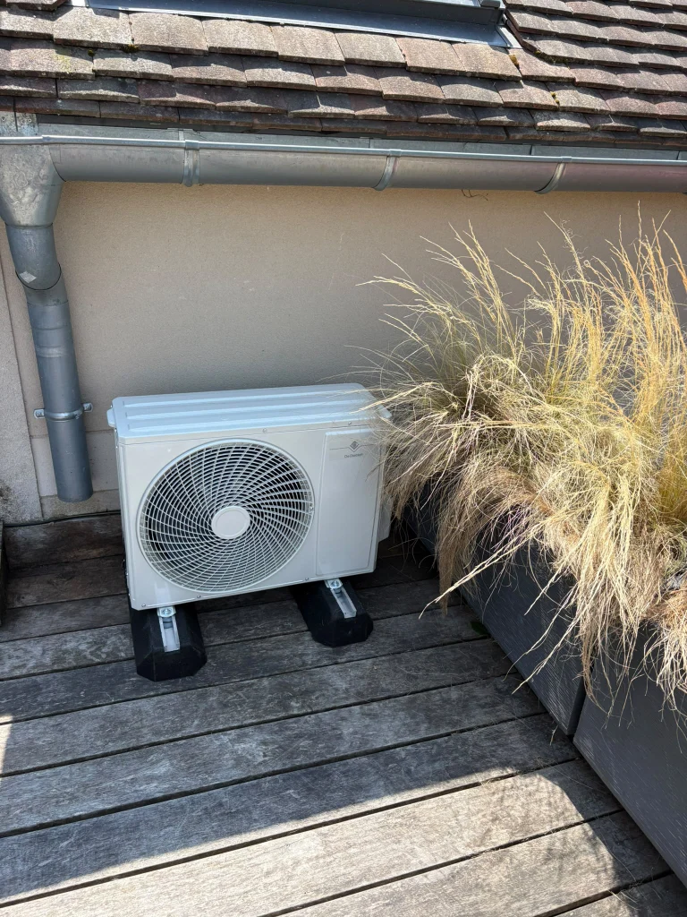 Groupe extérieur de climatisation sur une terrasse en bois entre des graminées, climaticien Île-de-France