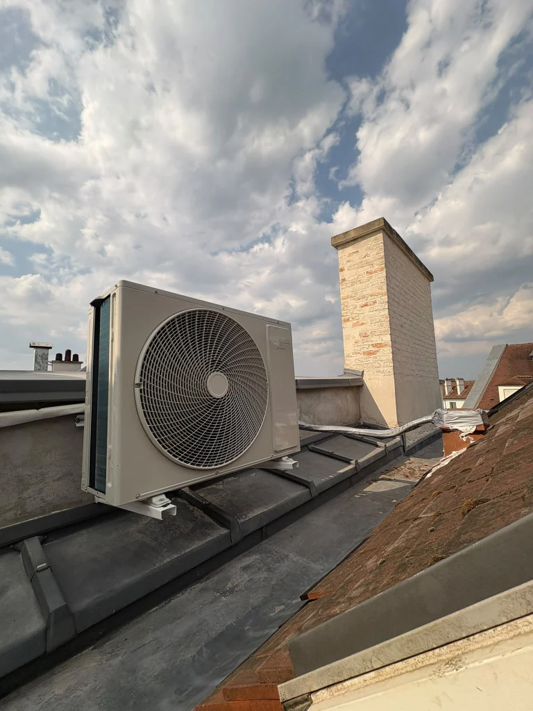 Groupe extérieur de climatisation posé sur une toiture en zinc entre les cheminées, climaticien Île-de-France