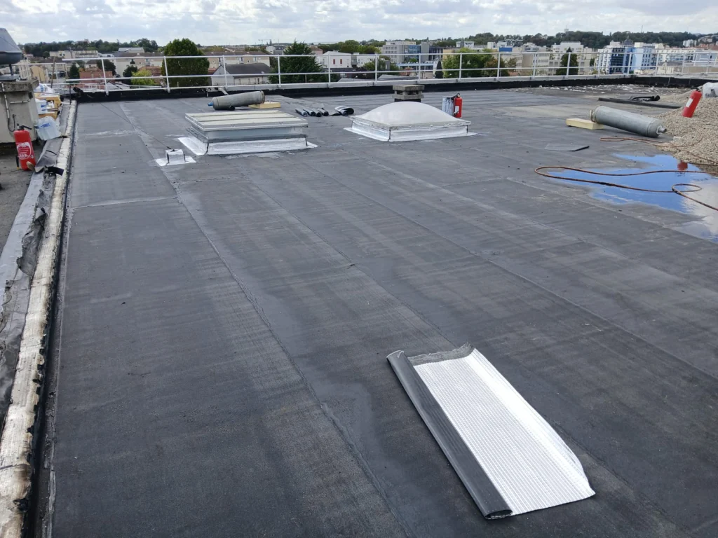 Toiture-terrasse d'immeuble refaite en bitume bicouche sous gravillons avec lanterneaux, étancheur Île-de-France