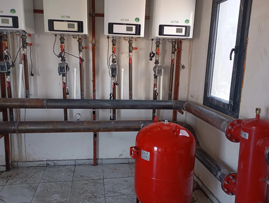 Chaufferie collective : trois chaudières gaz à condensation en cascade, bouteille de découplage rouge et vase d'expansion, chauffagiste Île-de-France