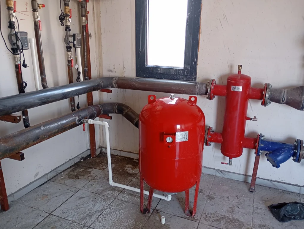 Chaufferie collective : trois chaudières gaz à condensation en cascade, bouteille de découplage rouge et vase d'expansion, chauffagiste Île-de-France
