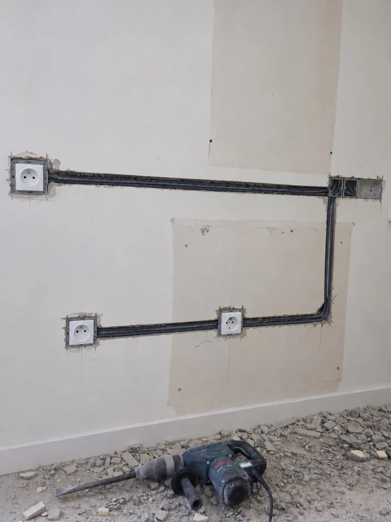Saignées dans un mur avec gaines encastrées reliant des boîtiers de prises neufs, perforateur au sol, rénovation de câblage électrique Île-de-France