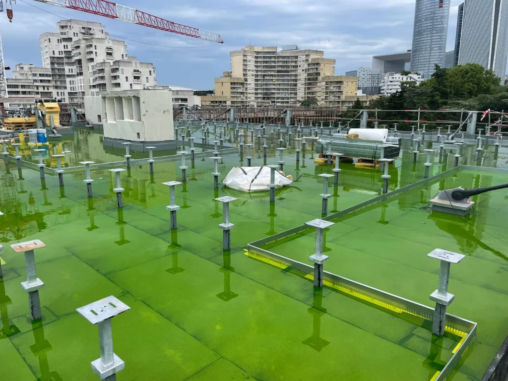 Grande toiture-terrasse neuve en mise en eau colorée avant pose des dalles sur plots, étancheur Île-de-France